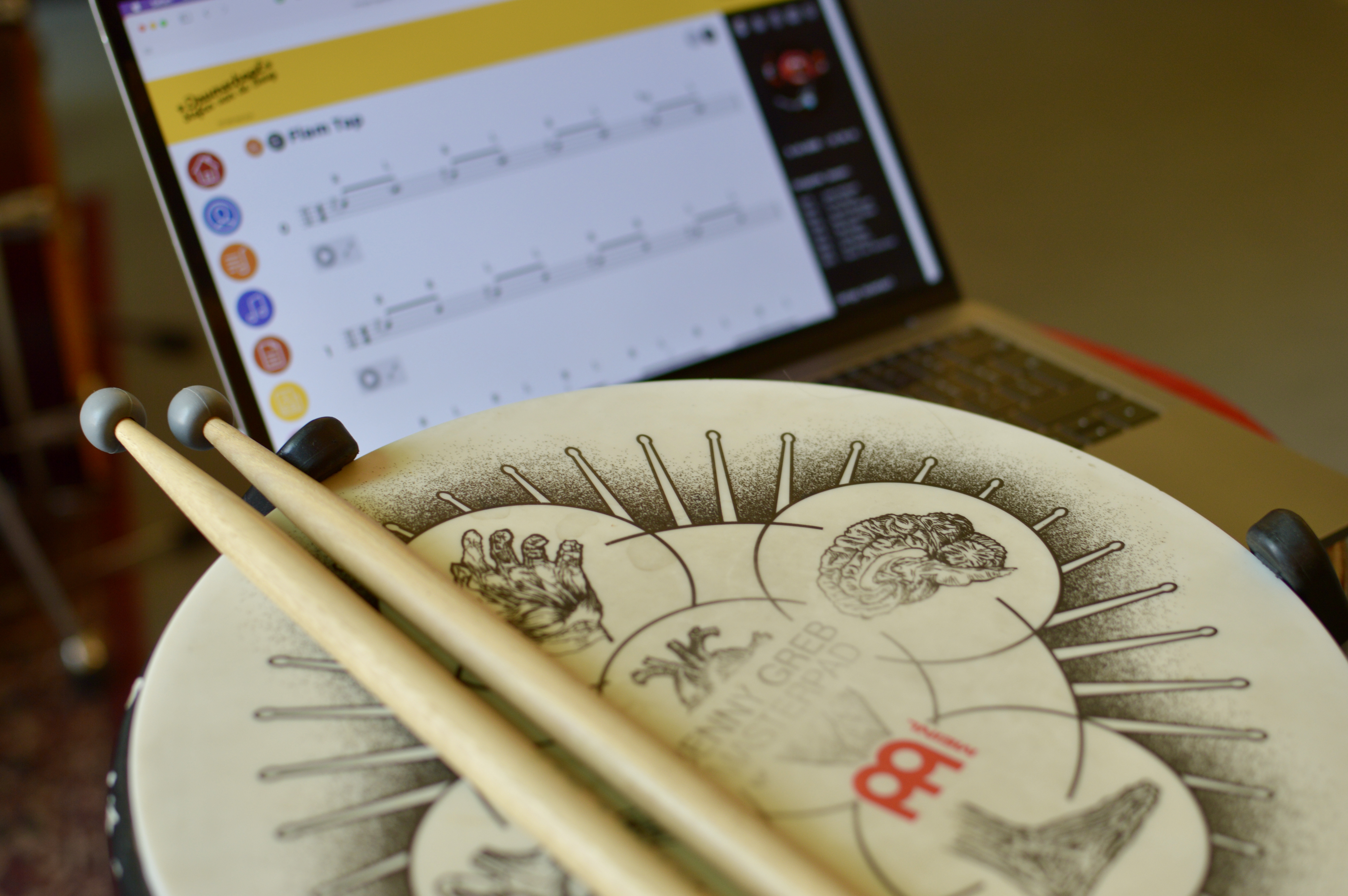 Practice pad met drumstokken en notatie op laptop